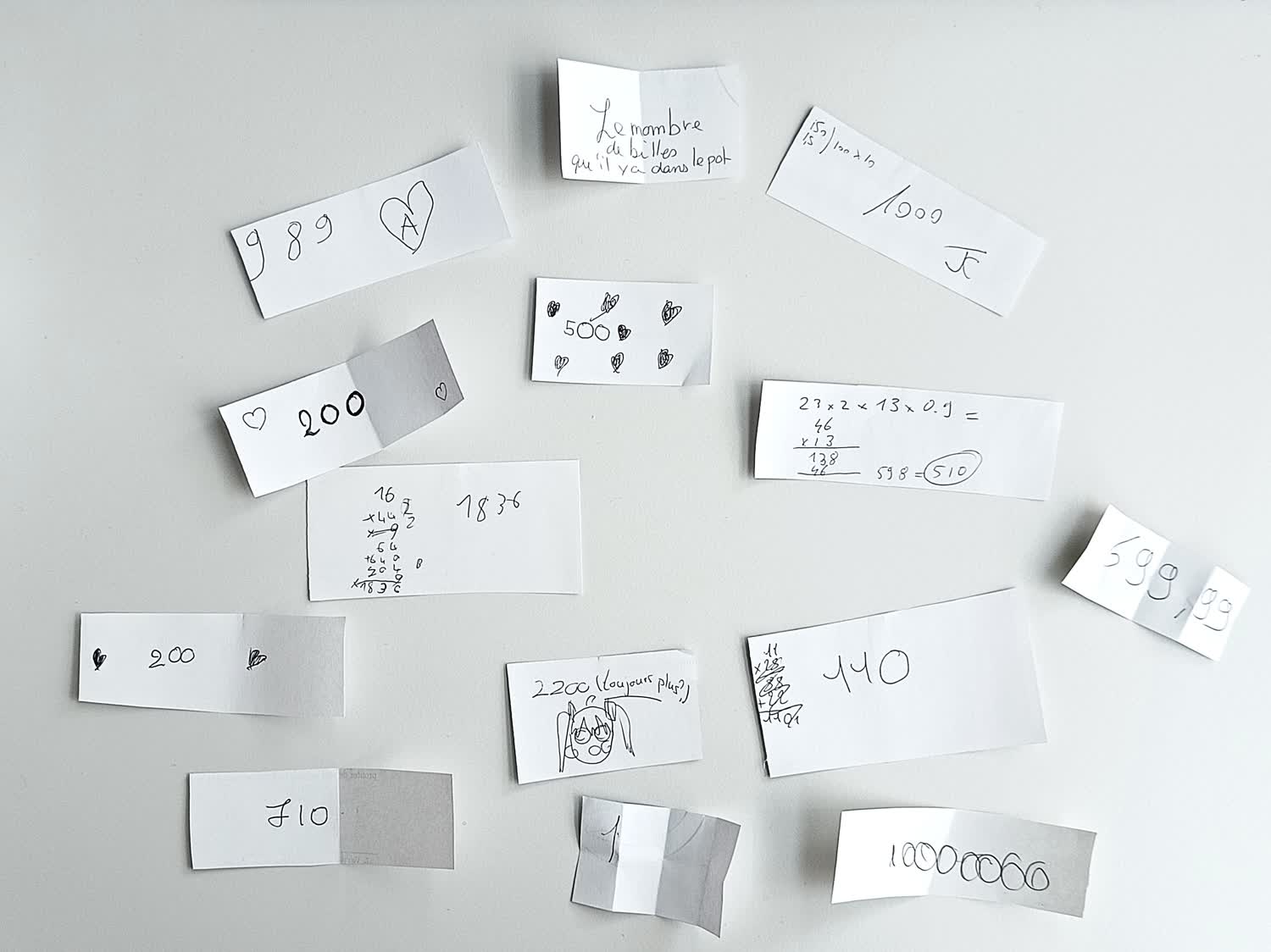 Photo de quelques bulletins, avec des dessins, des cœurs, 710 écrit sur l'un, 1 sur un autre, 10000000 sur un autre, « Le nombre de billes qu'il y a dans le pot » sur un autre.