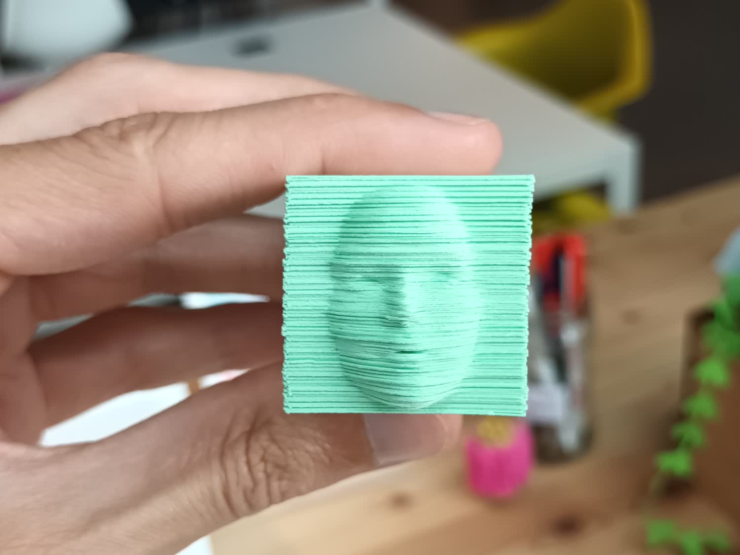 Une main tient un carnet d'une centaine de feuilles vertes découpées format un visage, face à la caméra.