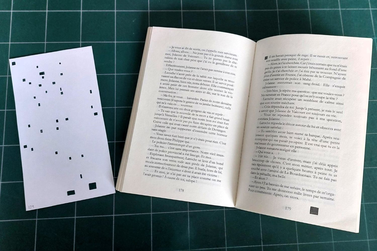Photo d'un livre ouvert à côté d'une feuille cartonnée avec quelques dizaines de trous carrés de la taille d'un caractère.