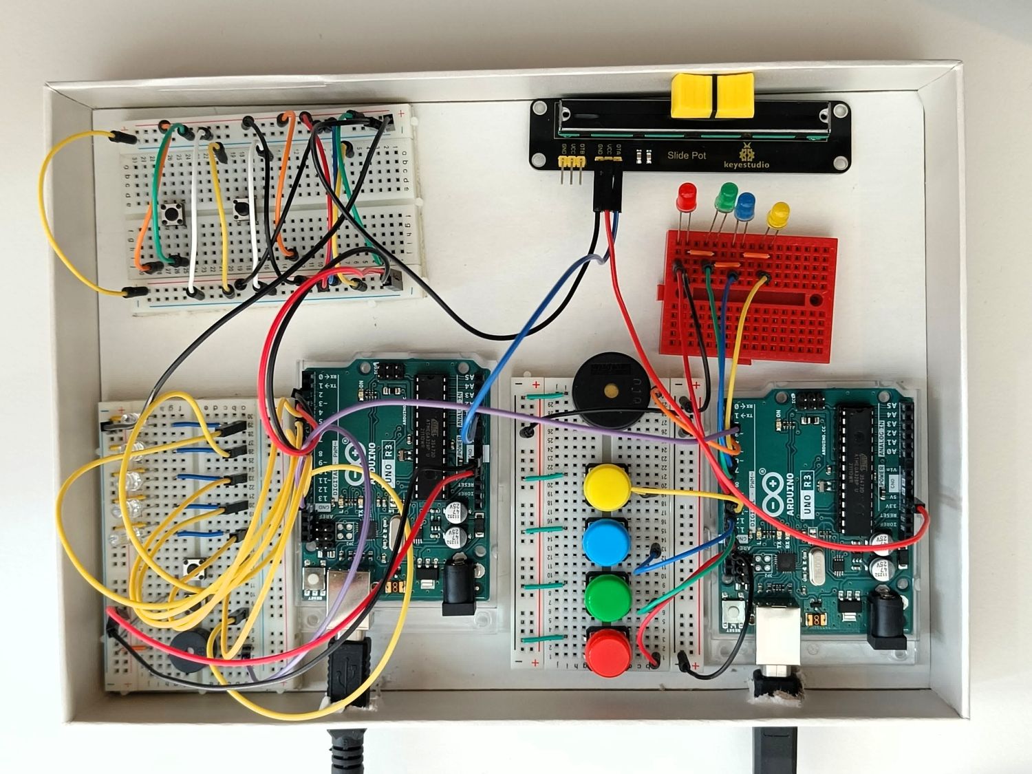 Photo du casse-tête vu de dessus : deux cartes Arduino, trois planches de prototypage avec beaucoup de fils, de LED de plusieurs couleurs, de boutons de plusieurs couleurs